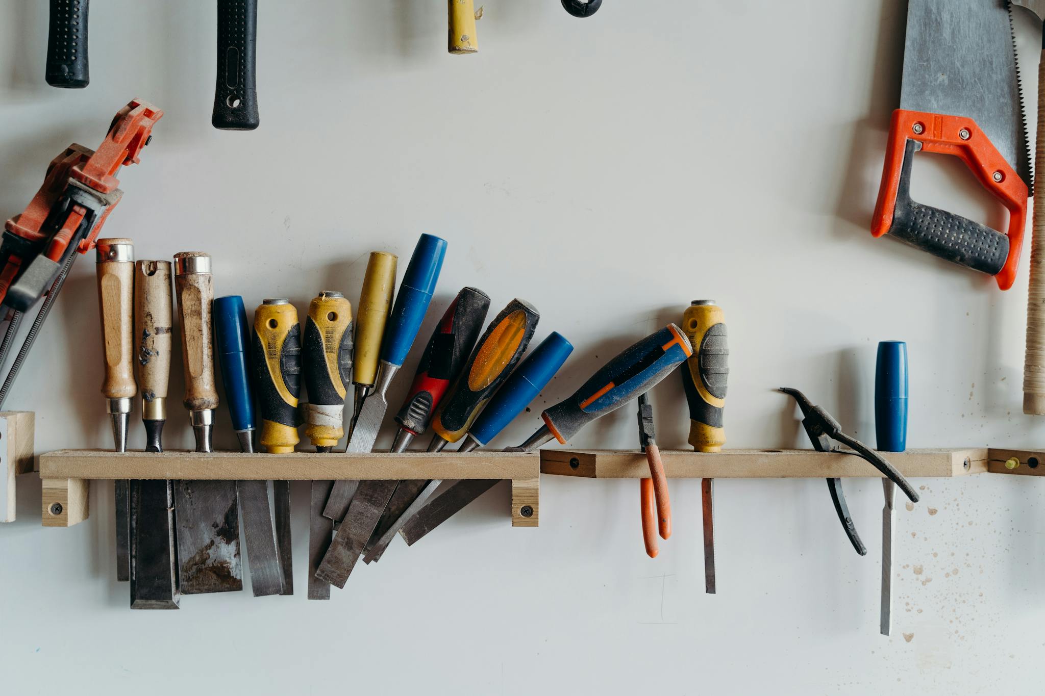 A neatly arranged collection of hand tools including chisels, saws, and screwdrivers in a workshop.